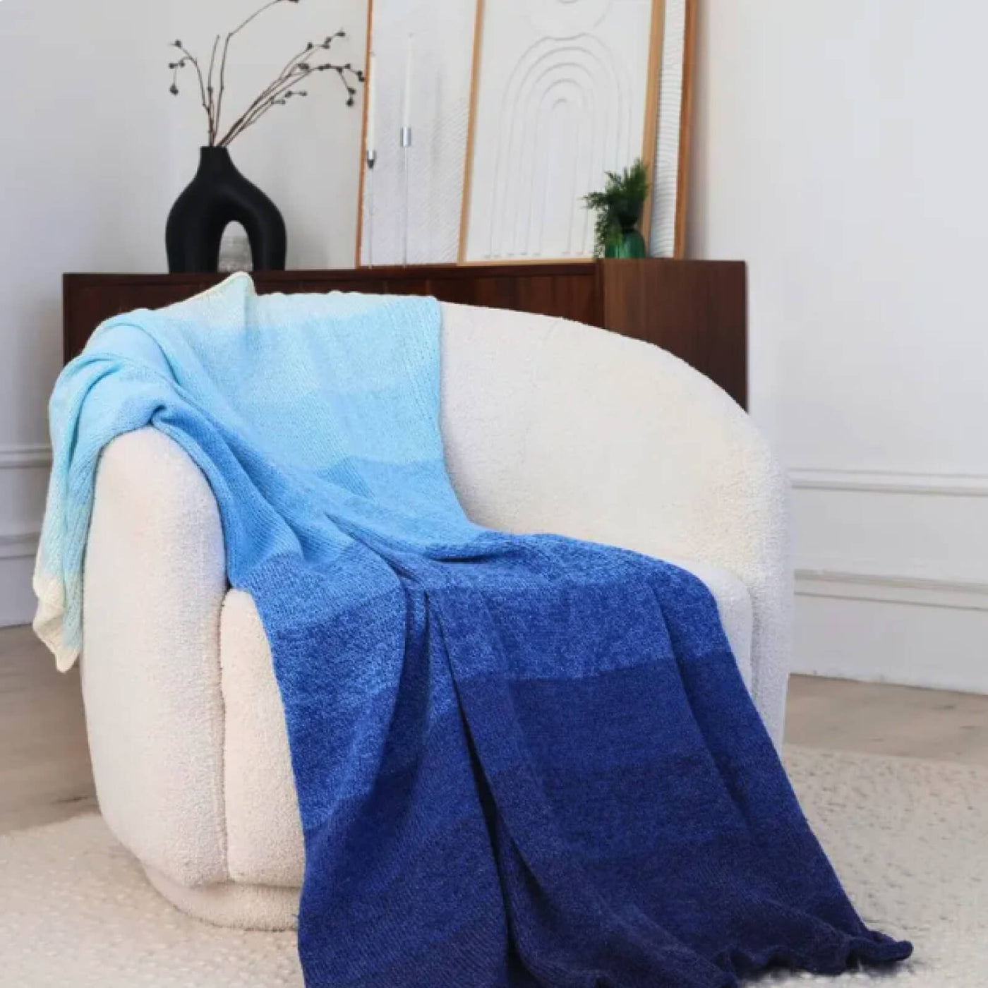 Blue blanket draped over a white armchair in a room with a vase and plant in the background.