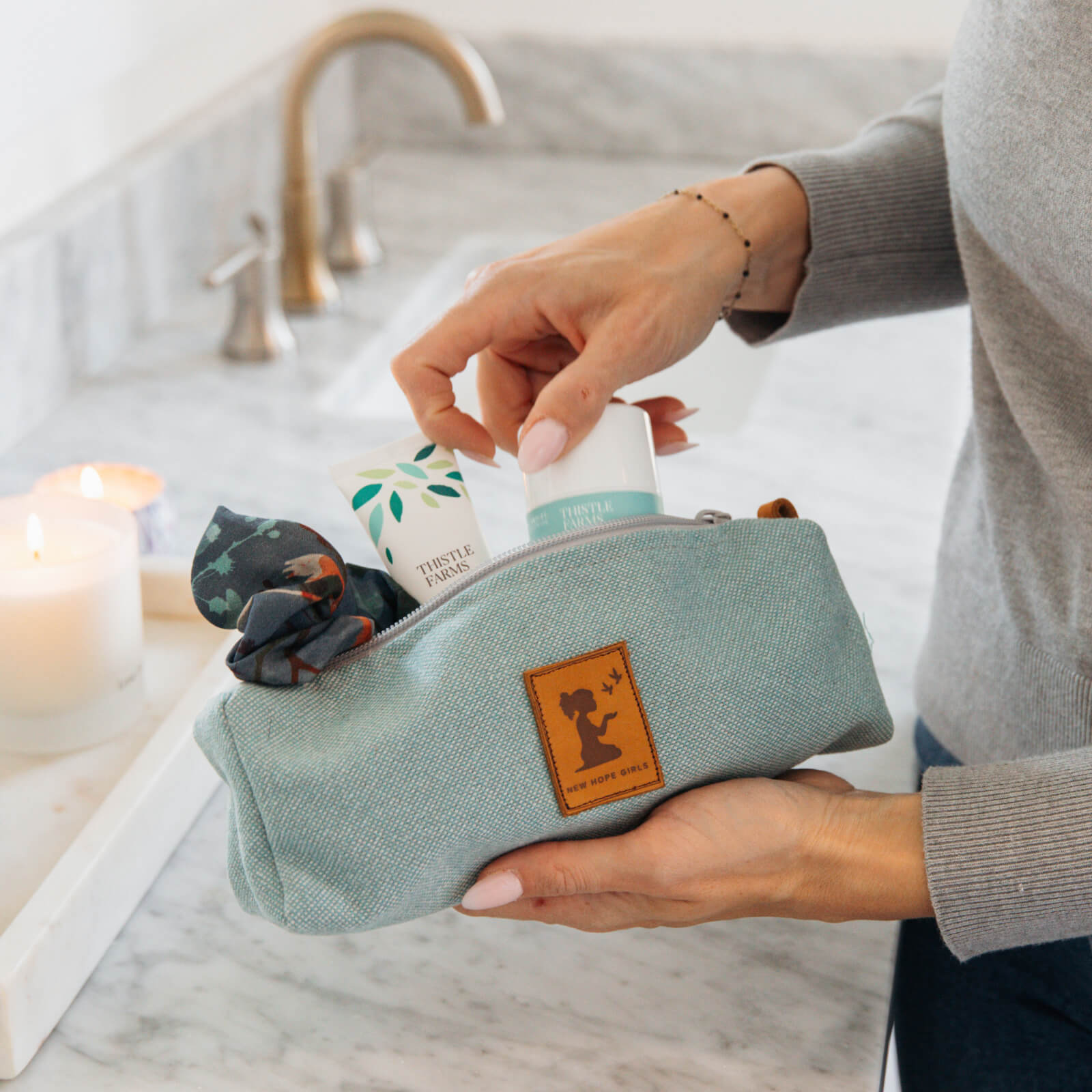 Person holding a light blue toiletry bag with products on a bathroom counter.