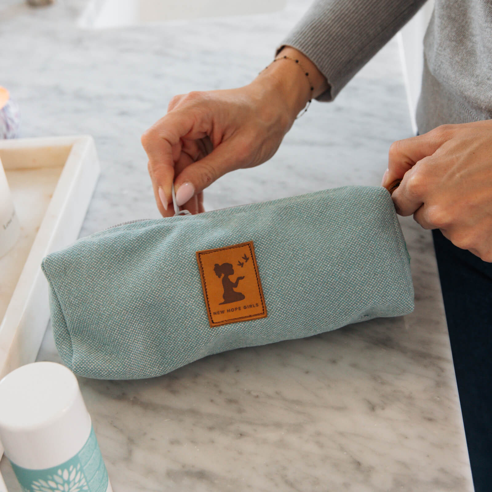 Person holding a light blue fabric pouch with a logo on a marble surface