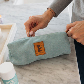 Person holding a light blue fabric pouch with a logo on a marble surface