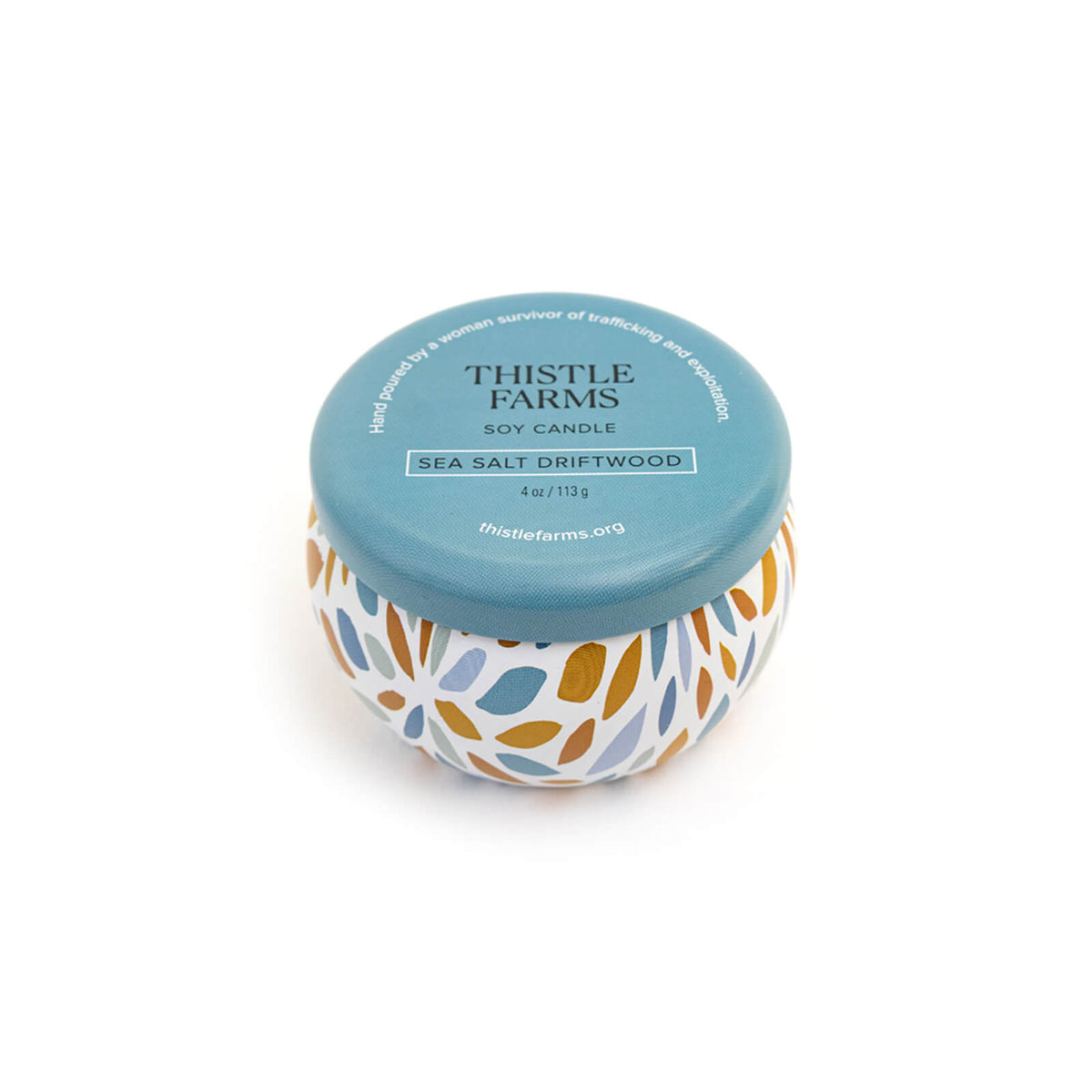 Candle jar with floral design and blue lid labeled 'Thistle Farms' on a white background