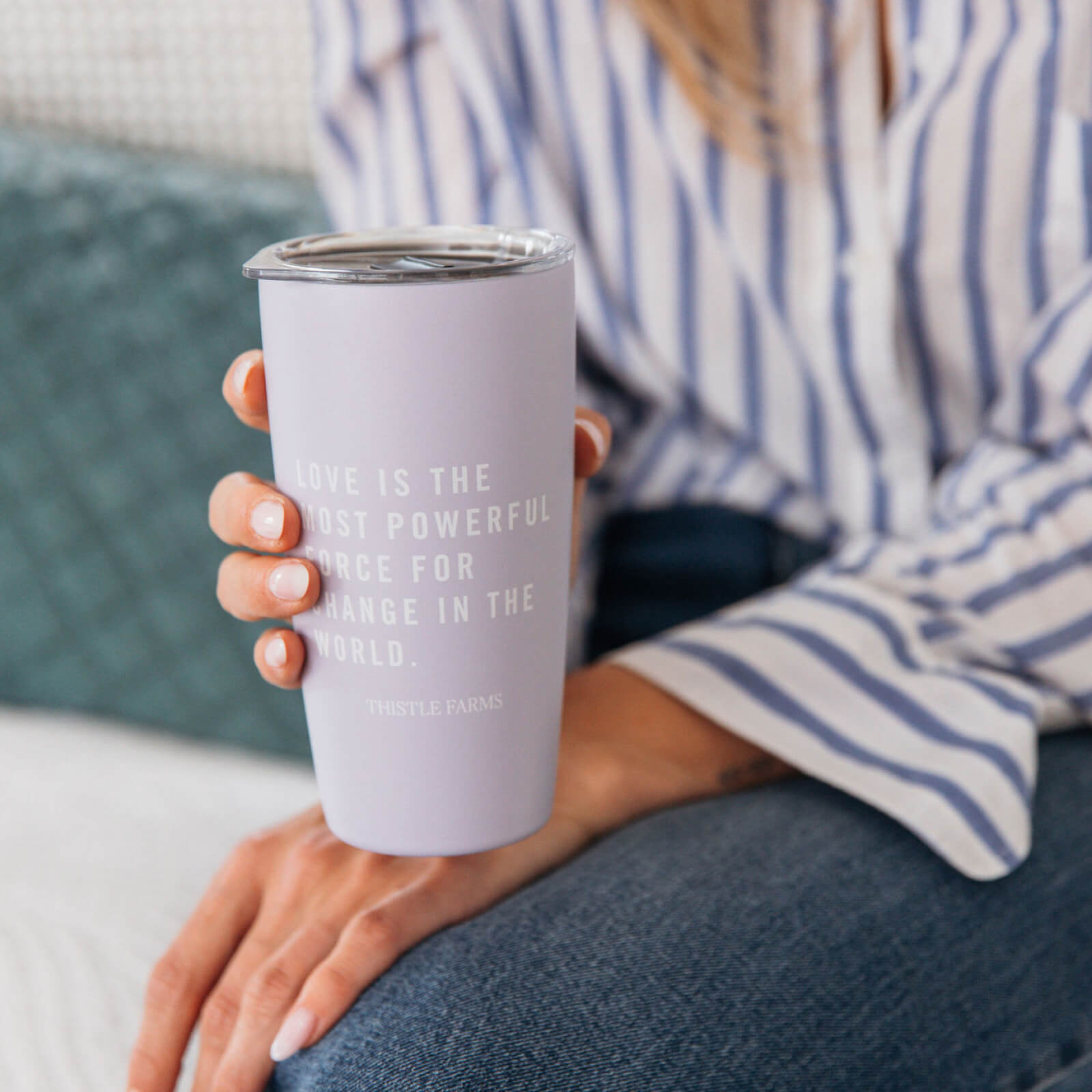 Person holding a lavender tumbler with text, sitting on a couch.
