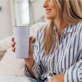 Woman holding a lavender tumbler with text, sitting on a couch.