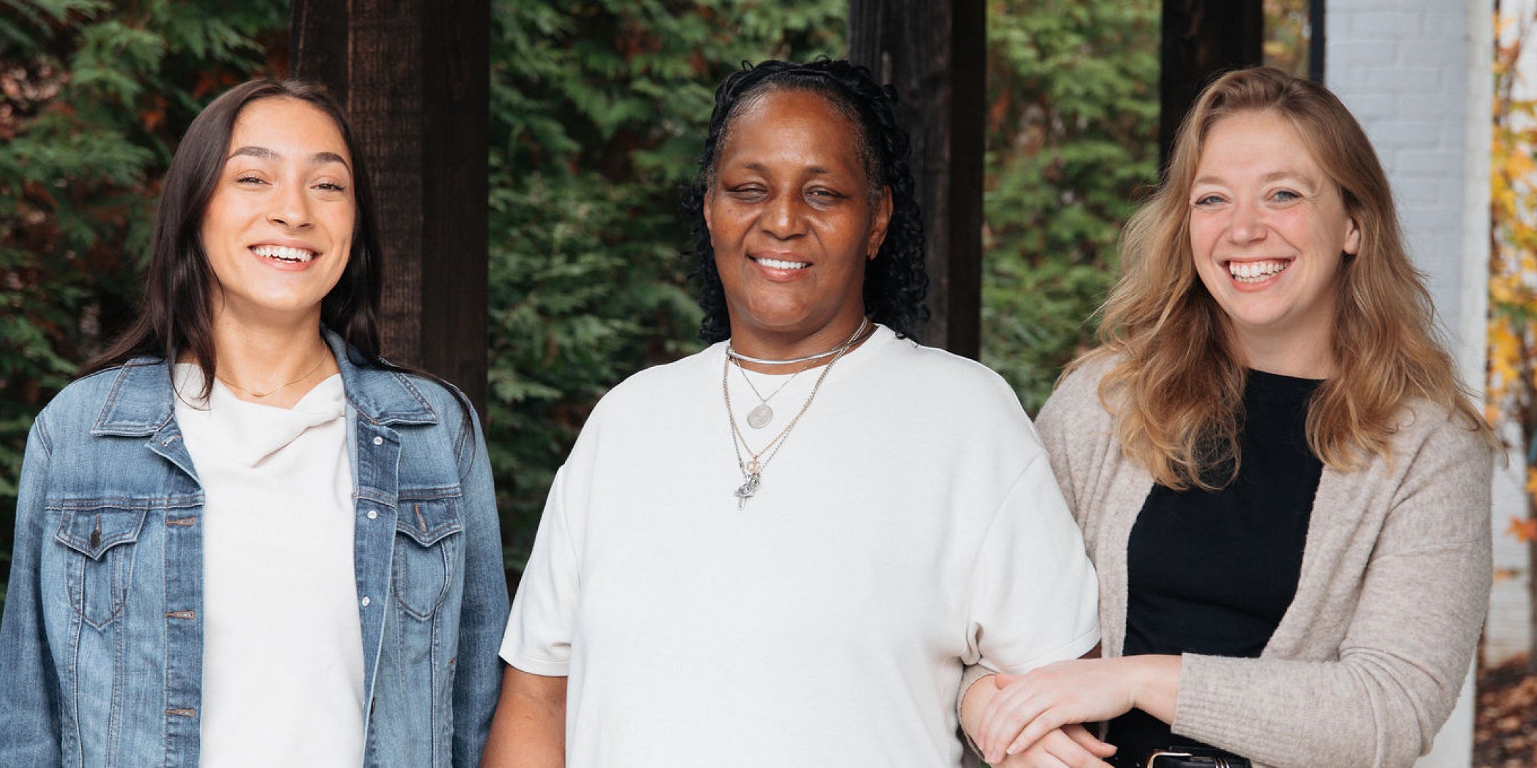 Three women standing together outdoors with trees in the background