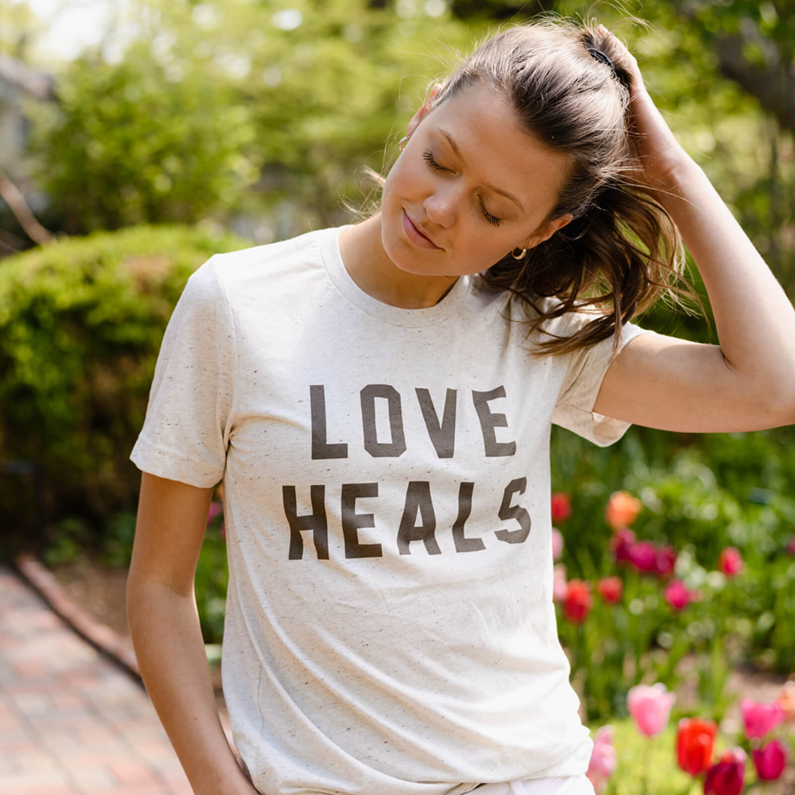 Woman wearing a 'LOVE HEALS' t-shirt in a garden setting
