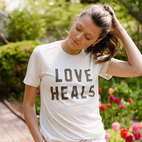Woman wearing a 'LOVE HEALS' t-shirt in a garden setting