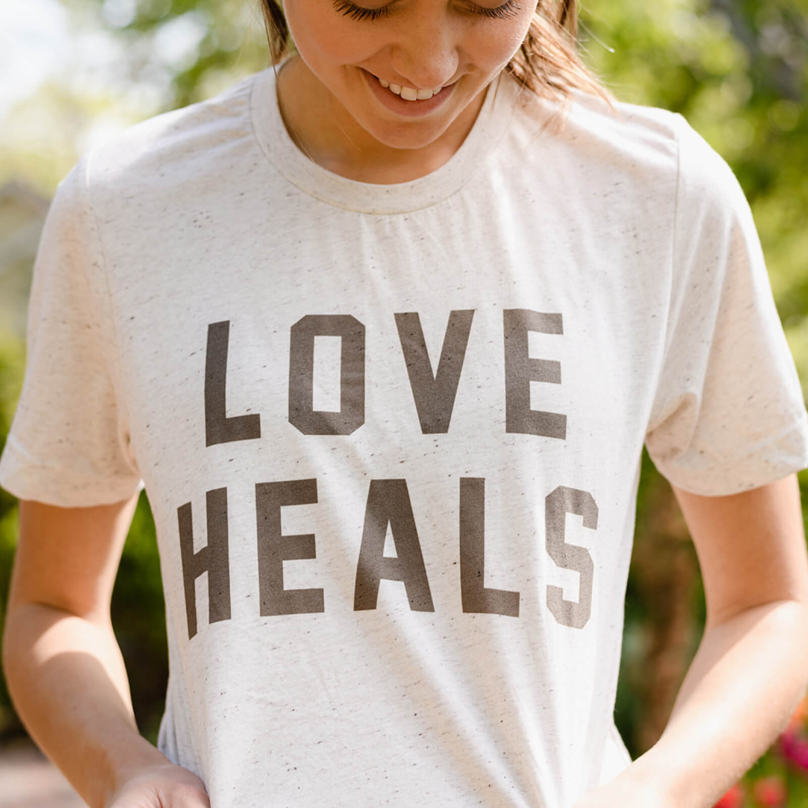 Person wearing a white t-shirt with 'LOVE HEALS' text in an outdoor setting