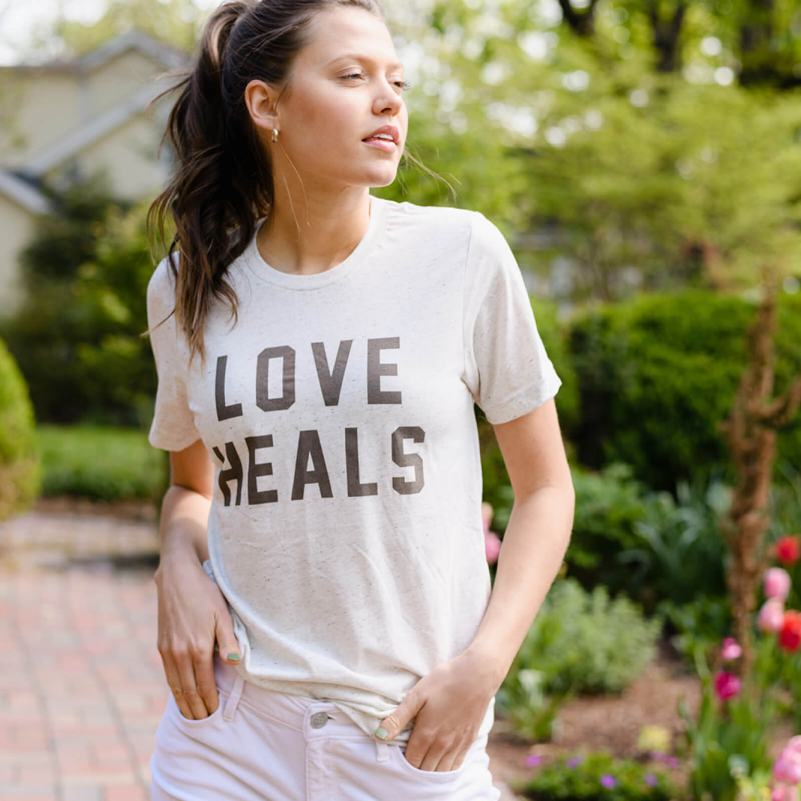 Woman wearing a 'LOVE HEALS' t-shirt in a garden setting