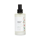 A white spray bottle labeled 'Thistle Farms Palo Santo Sage Room Mist' with a black cap, part of the 'love heals' collection.