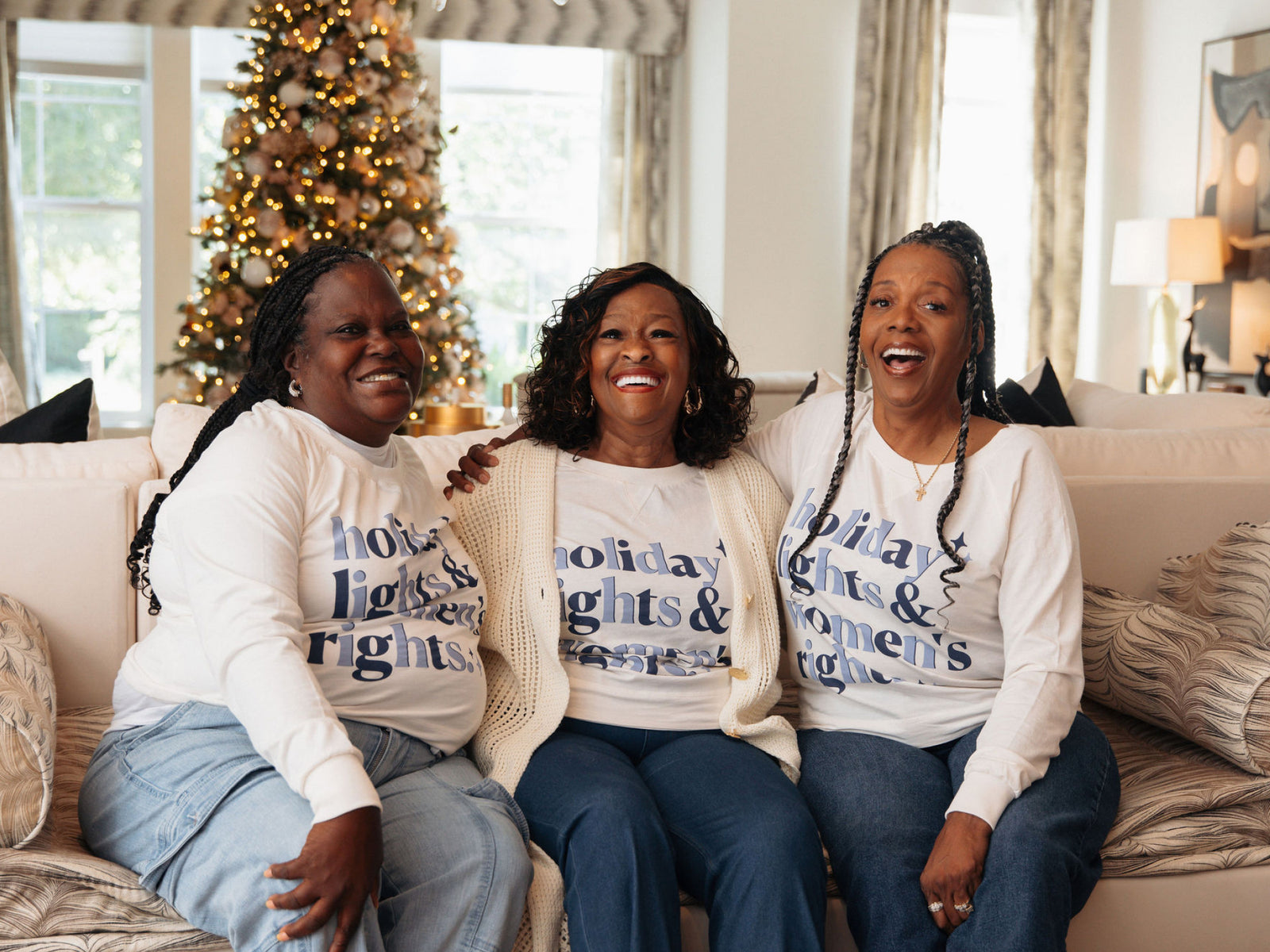 Three women sitting on a couch wearing matching holiday-themed sweaters in a cozy living room.