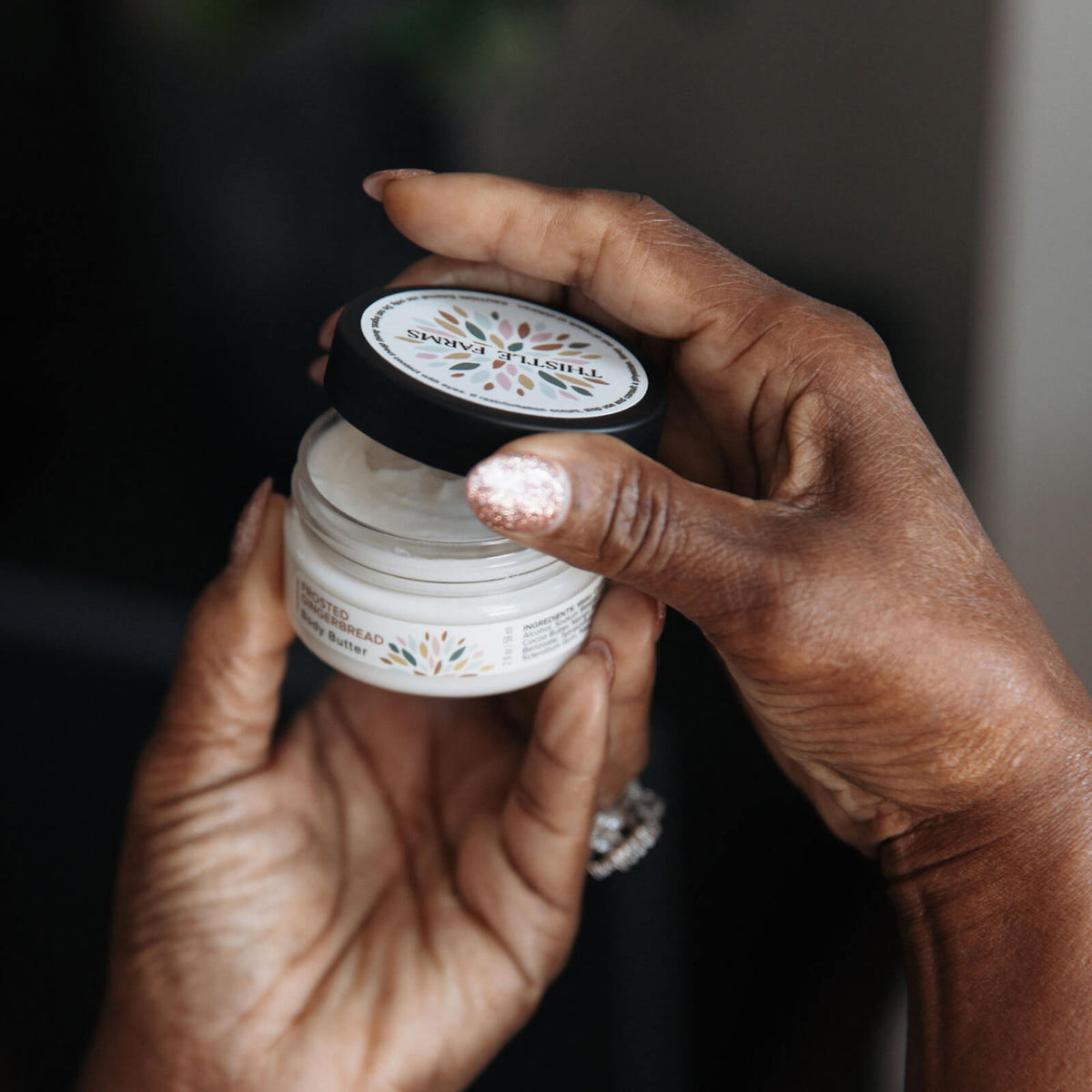 Two hands holding a jar of body butter with a blurred background