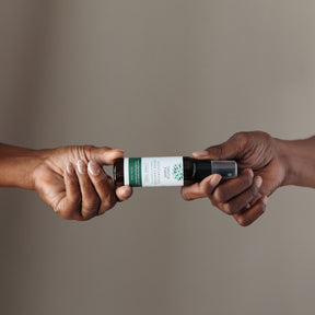 Two hands holding a hand sanitizer bottle with a green label against a neutral background