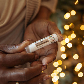 Lip balm held by hands with a blurred festive background