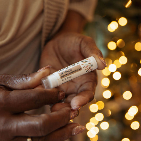 Lip balm held by hands with a blurred festive background