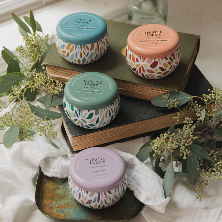 Four small jars with colorful lids on books, surrounded by greenery and fabric.