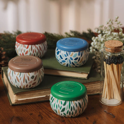 Set of four small jars with patterned lids on books, surrounded by a glass container with matches and decorative elements.