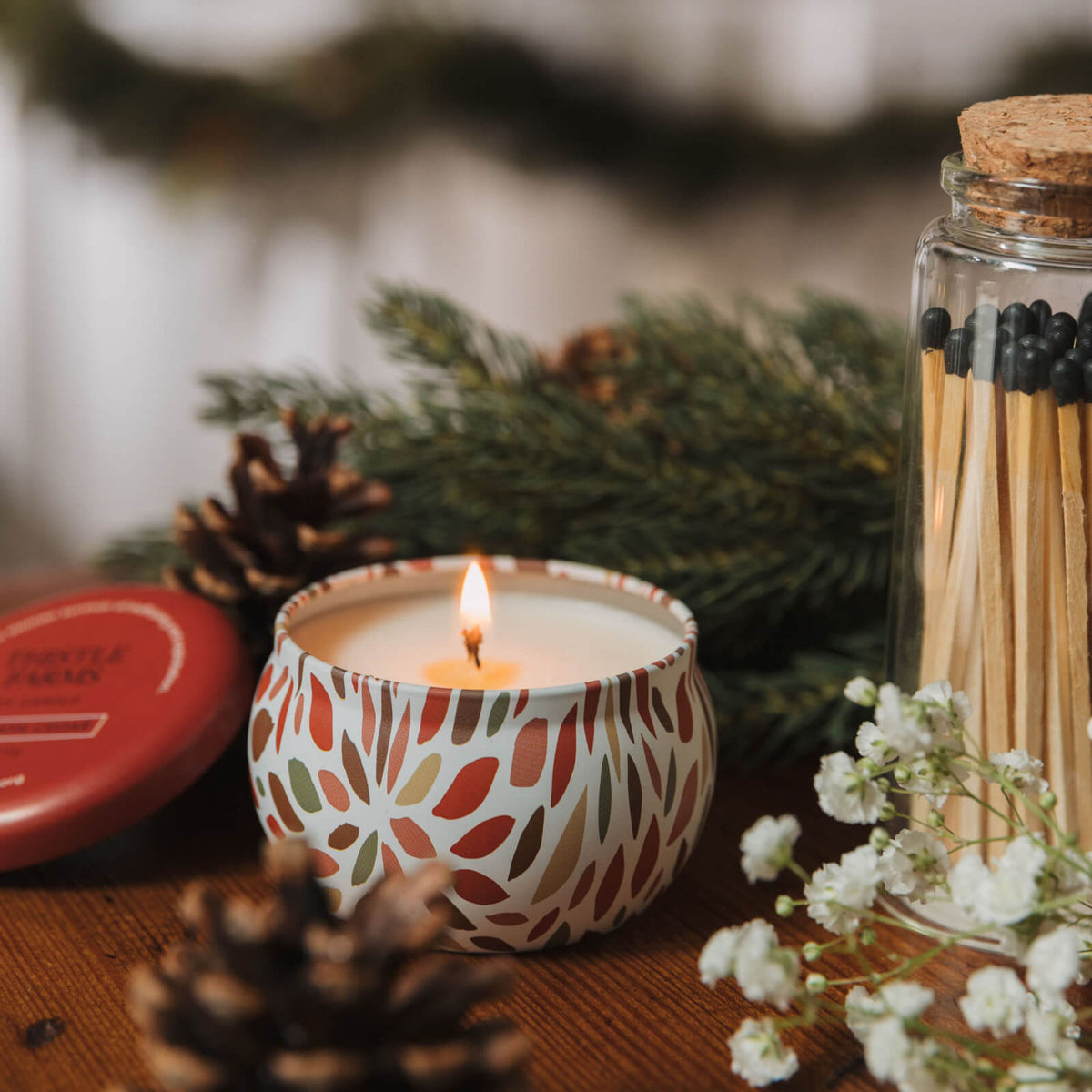 Red candle with decorative pattern, matches, and pinecones on a wooden surface