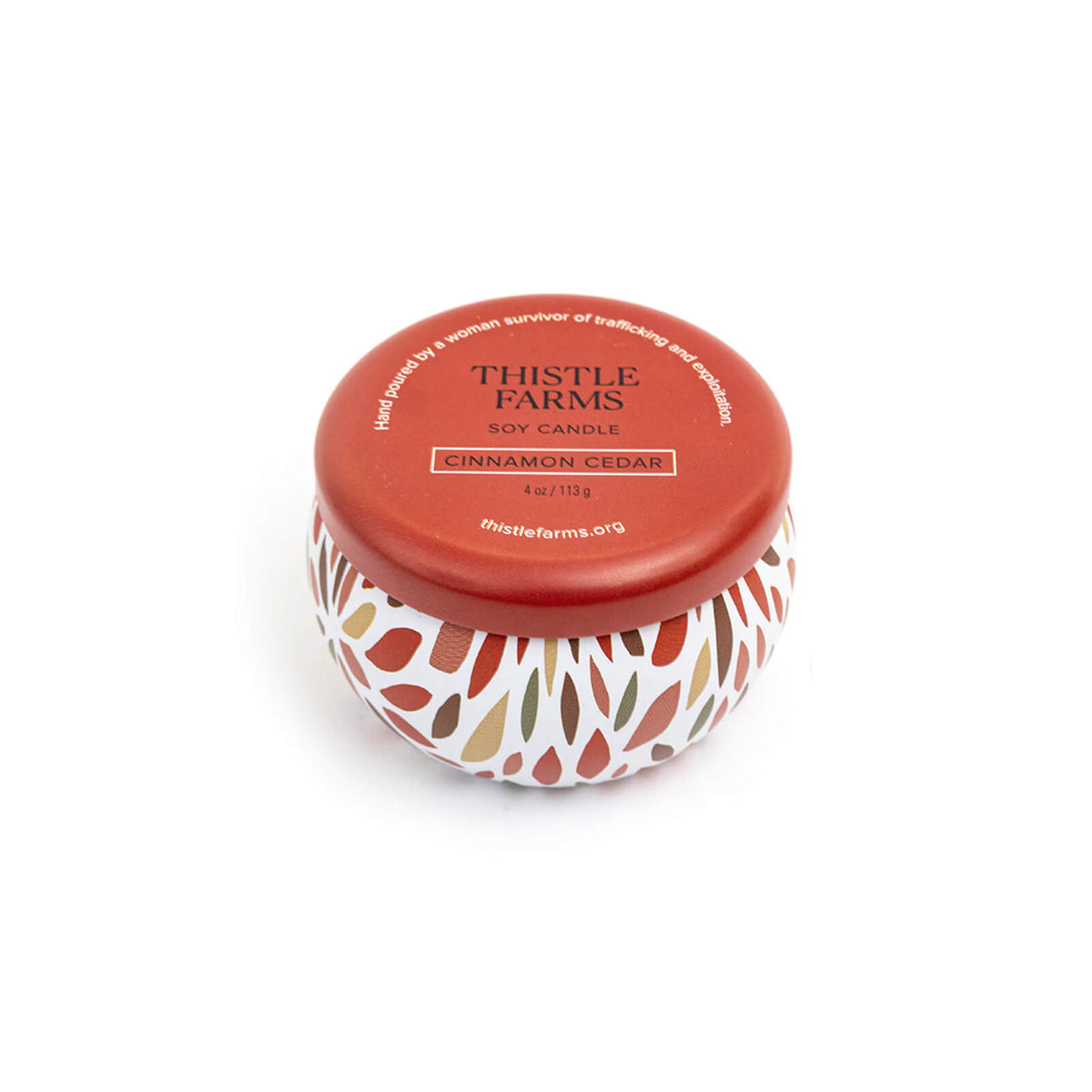 Thistle Farms candle with a leaf patterned base and red lid on a white background