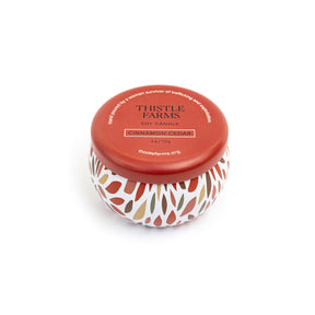 Thistle Farms candle with a leaf patterned base and red lid on a white background