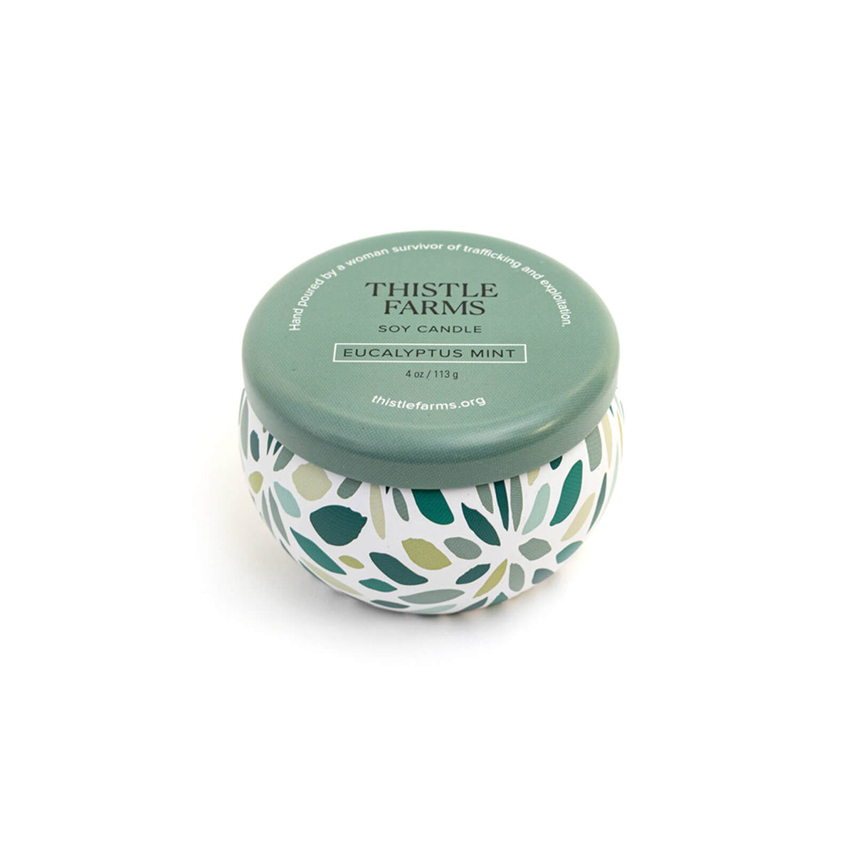 Thistle Farms soy candle with green lid and leaf patterned base on a white background