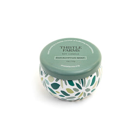 Thistle Farms soy candle with green lid and leaf patterned base on a white background