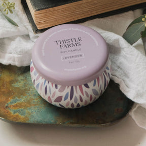 Thistle Farms soy candle with a purple lid on a decorative plate