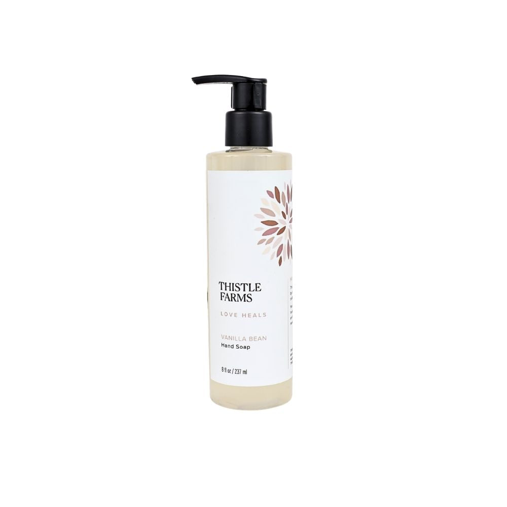 A bottle of Thistle Farms Love Heals Hand Soak in Vanilla Bean scent, featuring a white label with a brown floral design and a black pump dispenser, set against a plain white background.