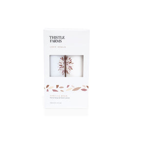 Thistle Farms Love Heals Vanilla Bean Hand Soap & Hand Lotion set in a white rectangular box with a clear window showing the white soaps inside, on a white background.