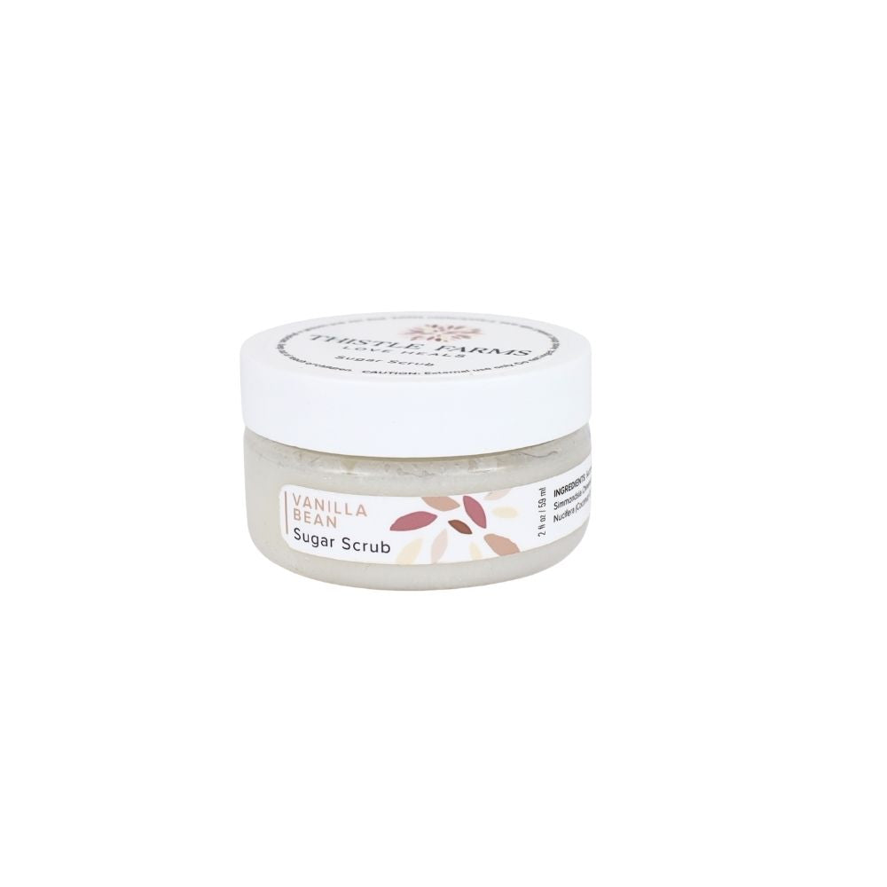 A small clear plastic jar of Vanilla Bean Sugar Scrub with a white screw-on lid and a white label featuring a floral design, set against a plain white background.