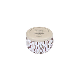 A round scented soy candle in a white container with a brown and gray leaf pattern, featuring a beige lid printed with 'THISTLE FARNES' and 'SOY CANDLE' on a plain white background.